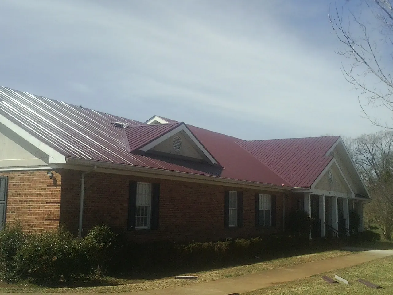 Red metal roof with gabled entries on a long brick building, from a Hail Damage Roof Repair job in Rutledge